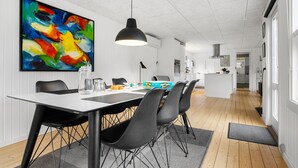 Una zona de menjador moderna amb una taula blanca, cadires negres i un quadre abstracte i colorit a la paret.
