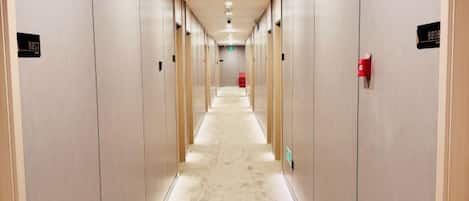 A hotel hallway with doors on both sides, a carpeted floor, and a fire extinguisher on the right.