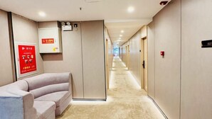 A hotel corridor with a sofa, a fire safety poster, and a digital display on the wall. - Keyuan hotel (Beijing)
