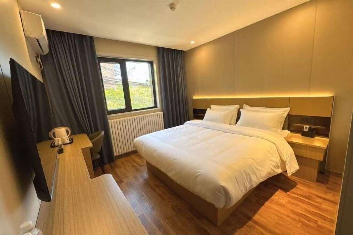 A modern hotel room with a large bed, bedside tables, a desk, and a window with curtains.
