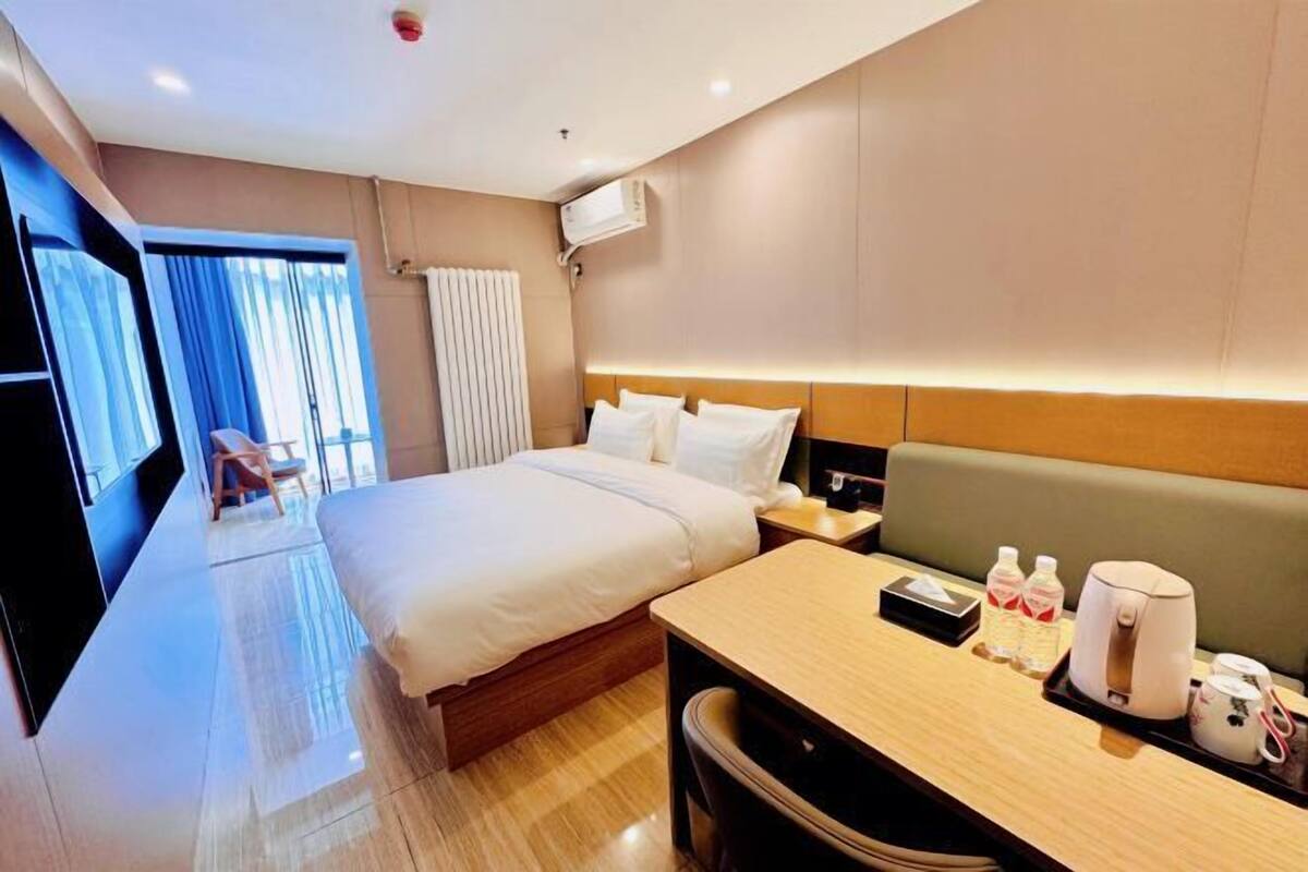 A hotel room with a large bed, bedside tables, a desk with a chair, and a view of the outdoors.