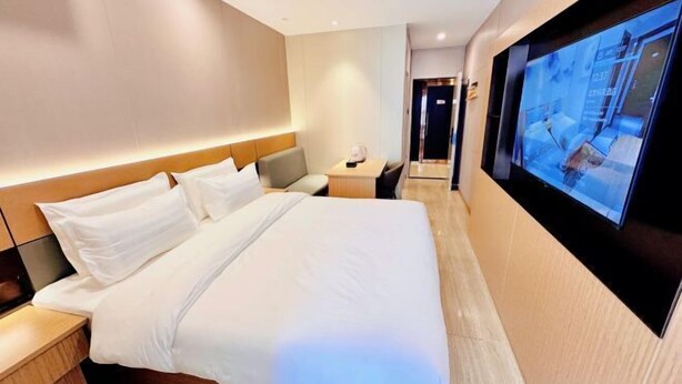 A modern hotel room with a large bed, a bedside table, a flat-screen TV mounted on the wall, and a hallway leading to the elevator. - Keyuan hotel (Beijing)
