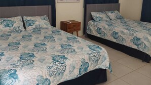 Een hotelkamer met twee bedden, een klein houten nachtkastje, een airconditioner en een muur met een poster van een strandthema.