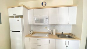 Een kleine keuken met witte kastjes, een magnetron, een broodrooster en een spoelbak.