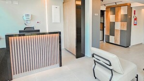 A modern reception area with a reception desk, a seating area with a white sofa, and a check-in counter. - Flat in Boa Viagem (2 km from the airport) (Boa Viagem Recife)