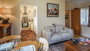 Una sala de estar acogedora con un sofá, una mesa de comedor para dos personas y una cocina al fondo.
