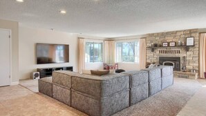 A living room with a large sectional sofa, a flat-screen TV, a fireplace, and large windows. - Fireplace, Soaking Tub & Peaceful Surroundings (Mariposa)