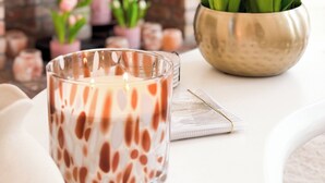 A candle with a heart pattern, a bowl of tulips, and a fireplace in the background.
