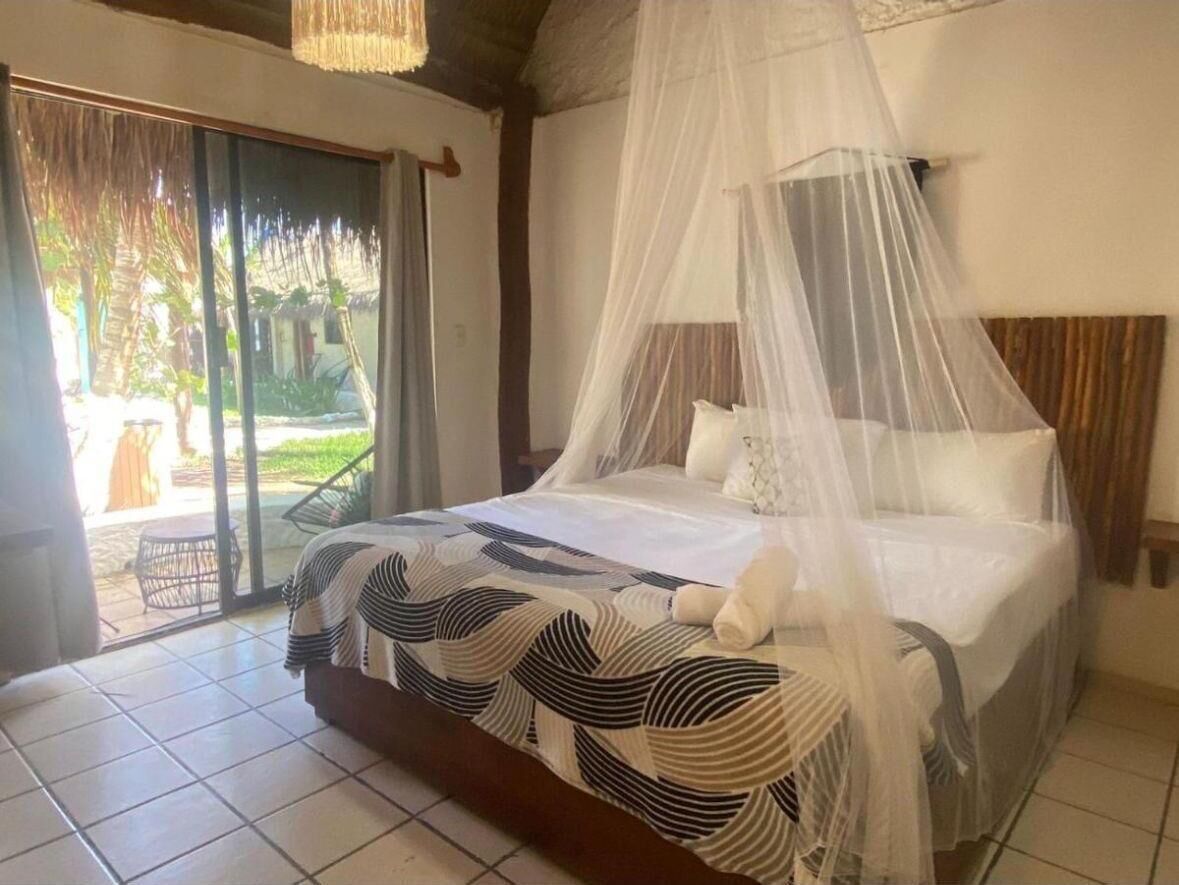 Un dormitorio con cama bajo dosel, vista al exterior a través de una puerta corrediza y suelo de baldosas.
