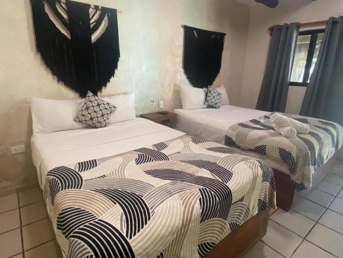 Two beds with patterned bedding, a wall hanging, and a window with curtains.
