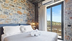 Un dormitorio con pared de piedra, cama con ropa de cama blanca y vista al campo a través de un ventanal.