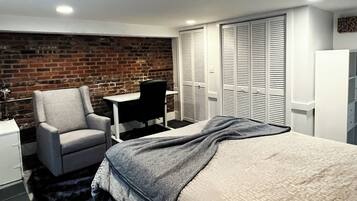 A bedroom with a brick wall, a desk, a chair, a bed, and a wardrobe.