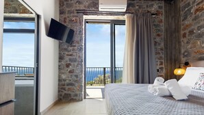 A bedroom with a large bed, a flat-screen TV, a balcony with a view, and a stone wall.