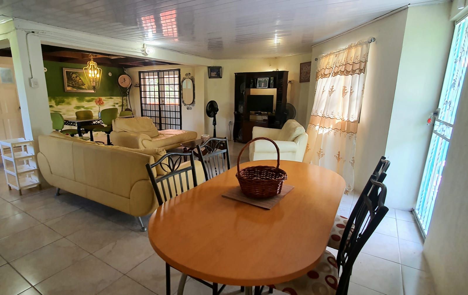 A living room with a sofa, a dining table with chairs, a TV, and a window with curtains.