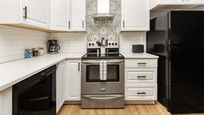 A modern kitchen with white cabinets, a black refrigerator, and stainless steel appliances.