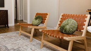 Two wooden lounge chairs with woven backs and cushioned seats, placed on a patterned rug in a room with a wooden floor and a white door in the background.