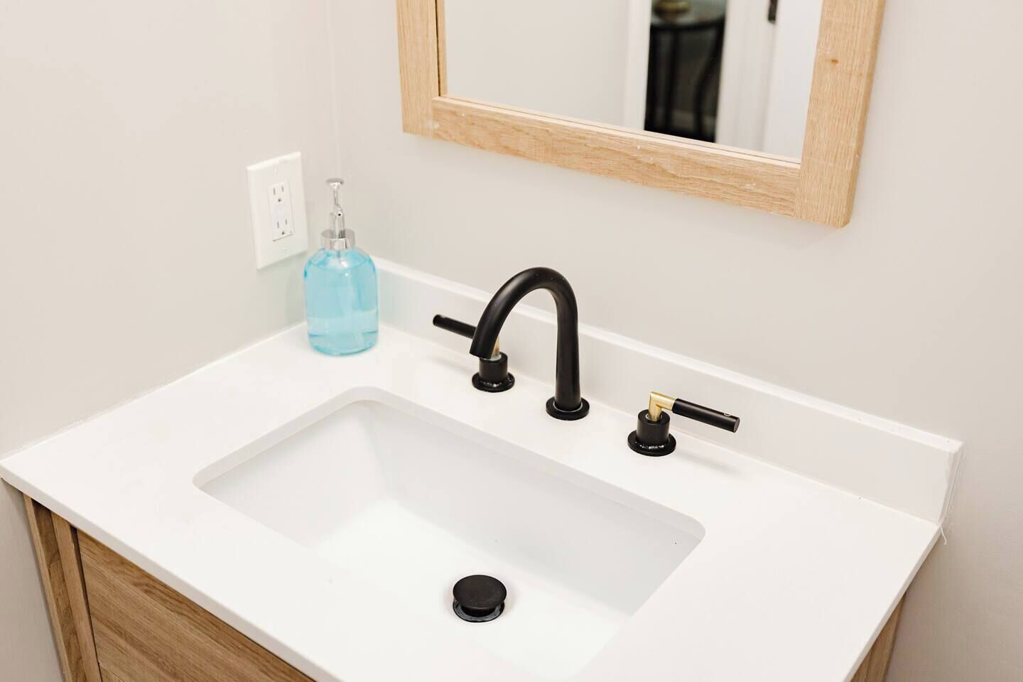 A white bathroom sink with a black faucet, a soap dispenser, and a mirror above it.