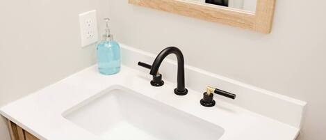 A white bathroom sink with a black faucet, a soap dispenser, and a mirror above it.