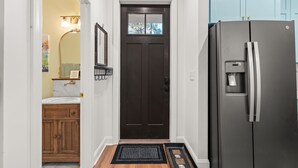 A hallway with a dark brown door, a refrigerator, wooden cabinets, and a marble countertop.