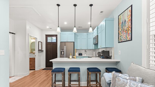 A modern kitchen with light blue cabinets, a central island with stools, and pendant lighting.