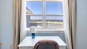 A room with a white desk, a blue lamp, and a view of a building and trees through a window with beige curtains. - The Perfect Brule Shore Getaway (Brule Shore)