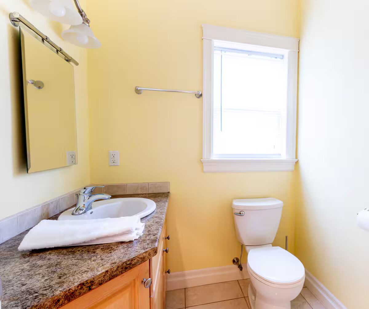 Une salle de bain avec un comptoir en granit, un lavabo blanc et des toilettes.