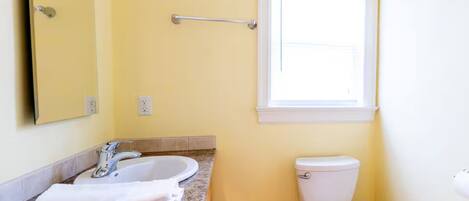 Une salle de bain avec un comptoir en granit, un lavabo blanc et des toilettes.