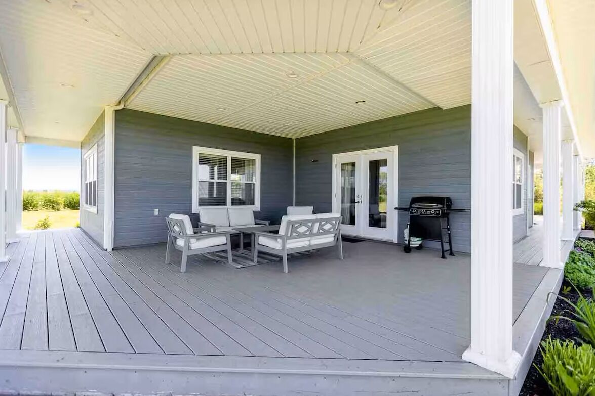 Eine überdachte Veranda mit Tisch und Stühlen, einem Grill und Blick ins Freie.