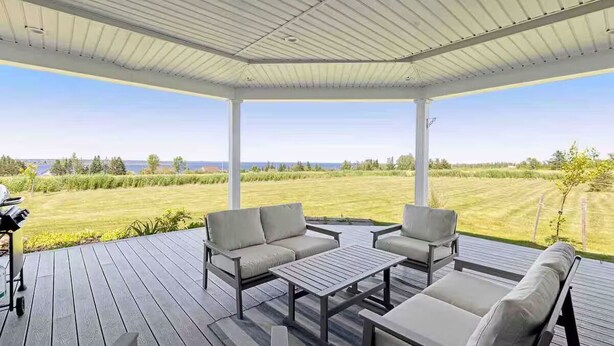 A covered outdoor patio with a view of a grassy field and a body of water. - The Perfect Brule Shore Getaway (Brule Shore)