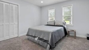 A bedroom with a bed, a nightstand, a window, and a closet.