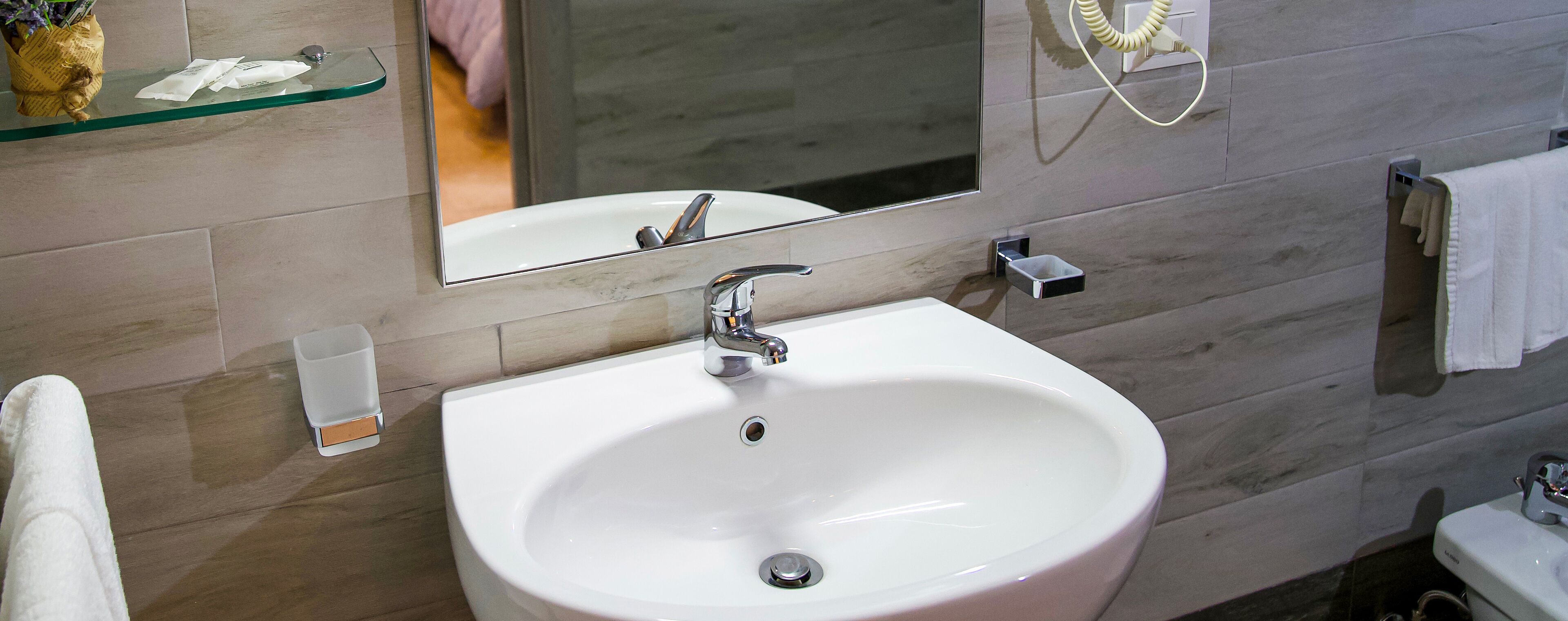 A bathroom with a white sink, a mirror, a towel rack, and a glass shelf with toiletries.