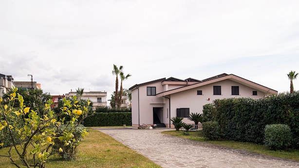 A modern residential building with a paved driveway, surrounded by well-maintained hedges and a small garden area. - Room to dream (San Valentino Torio)