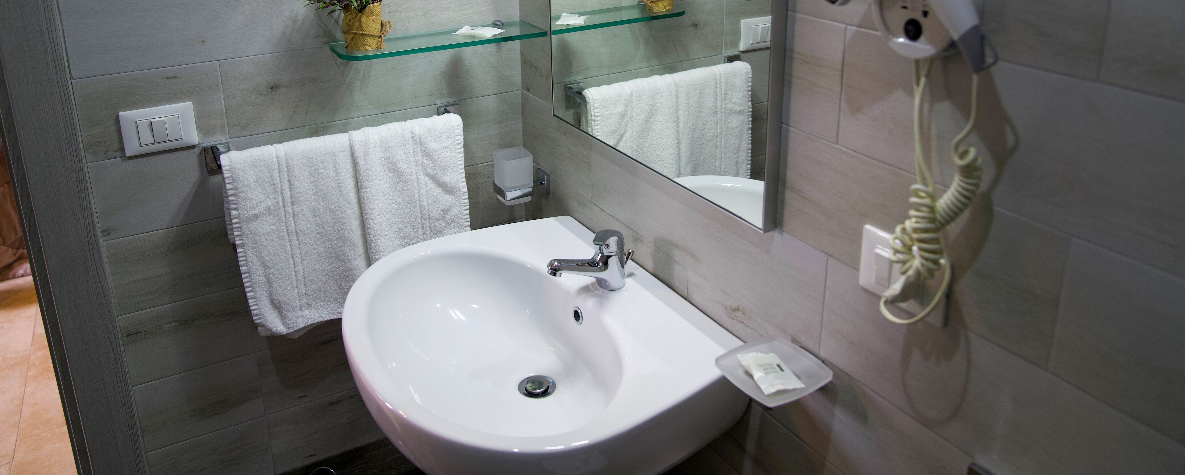 Une salle de bain avec un lavabo blanc, un miroir, un porte-serviettes et un sèche-cheveux.