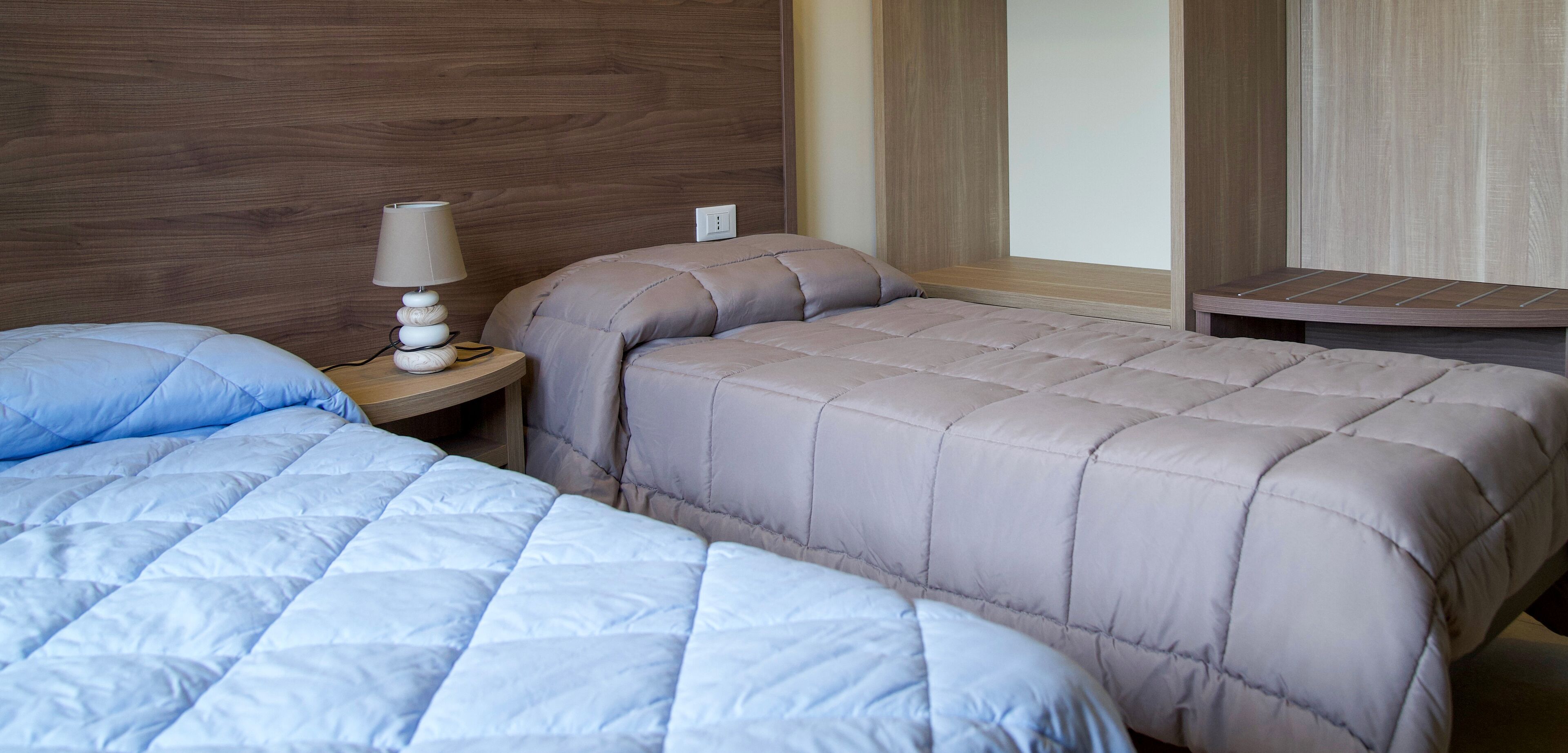 A hotel room with two beds, a nightstand with a lamp, and a wooden headboard.