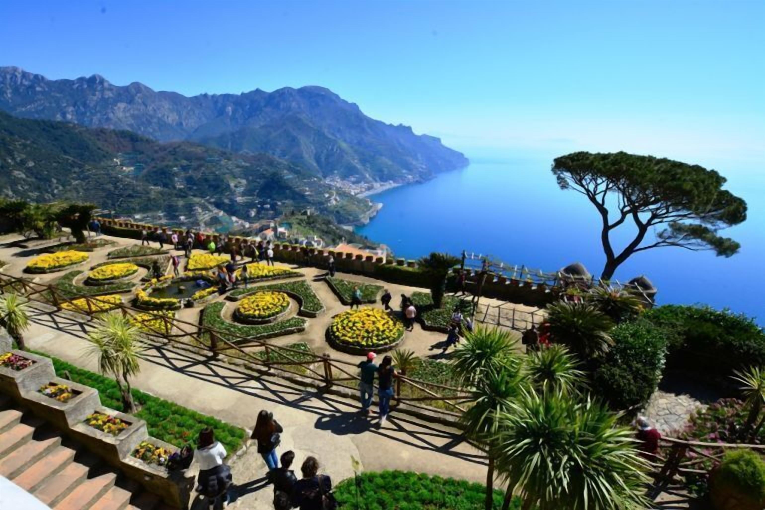 A garden with circular flower beds and a view of the sea and mountains.