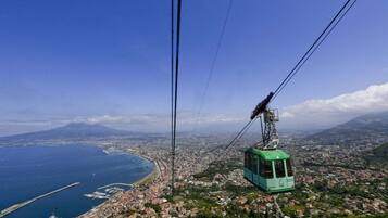 A cable car system with a green gondola, a coastal cityscape, and a mountain in the background.