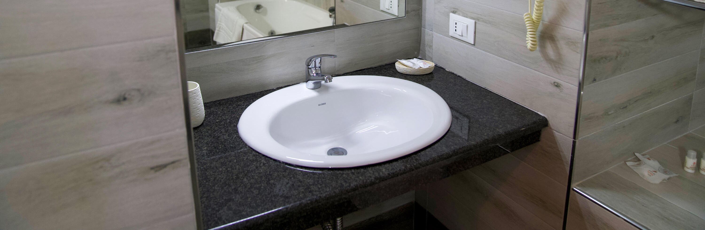 A white sink with a modern faucet, a mirror above it, and a small dish on the countertop.