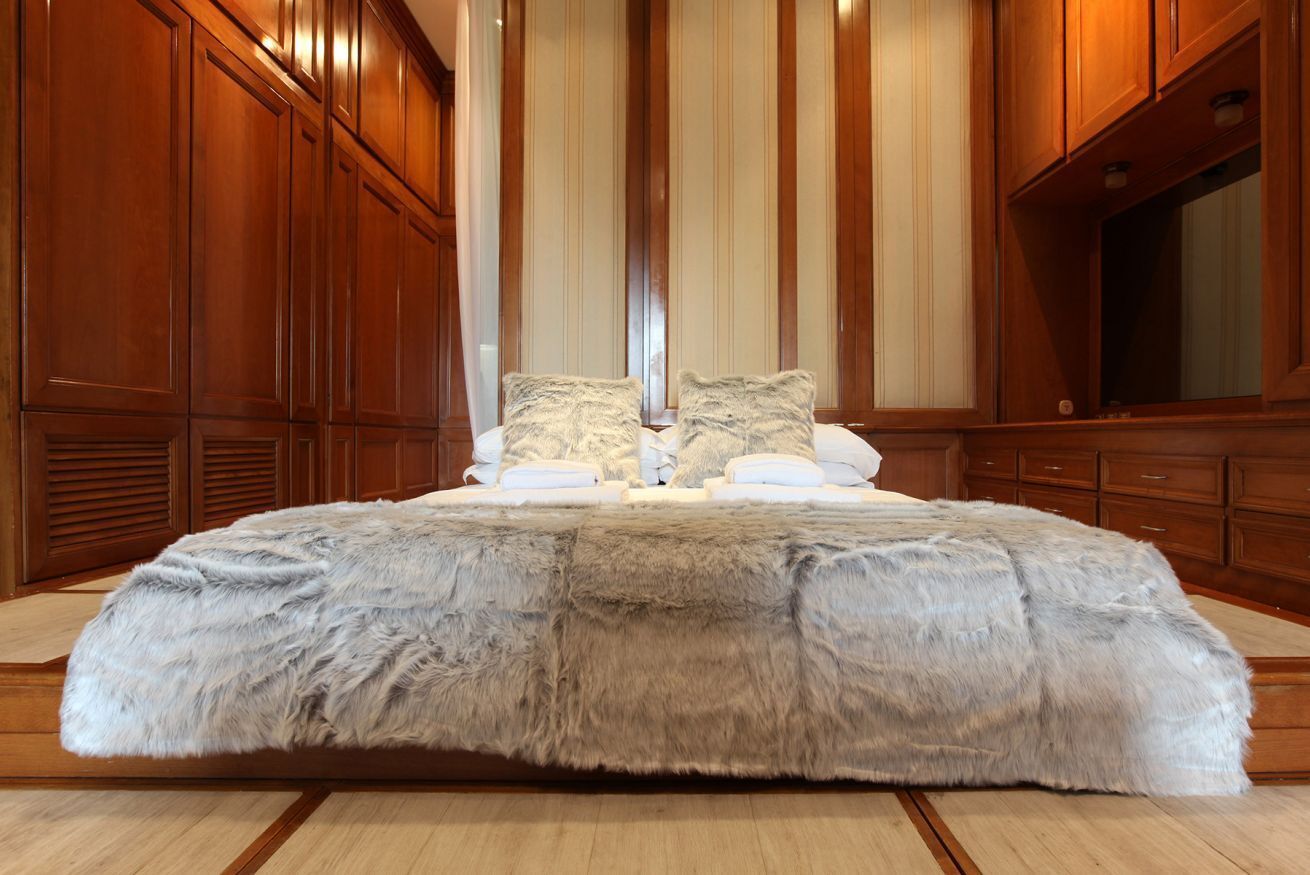 A large bed with a fluffy grey and white duvet, wooden paneling on the walls, and a large mirror on the right side.