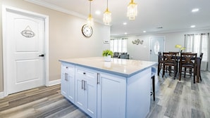 A modern kitchen with a central island, pendant lights, a clock, and a dining area with chairs. - Charming 3-bedroom house with AC and WiFi in awesome Kenner (Kenner)
