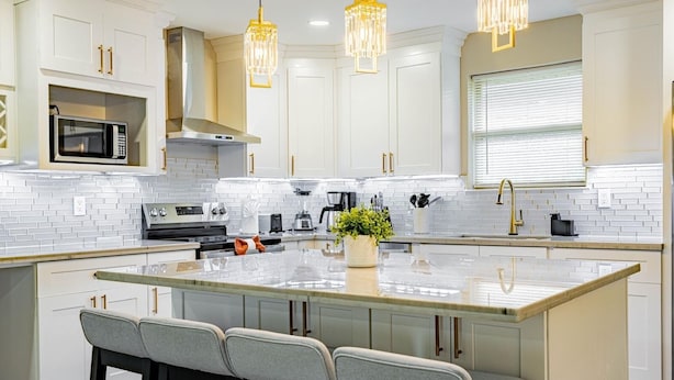 A modern kitchen with white cabinets, a large island, bar stools, a microwave, a stove, and pendant lights. - Charming 3-bedroom house with AC and WiFi in awesome Kenner (Kenner)