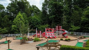 Un campo de mini golf con una estructura roja y blanca en el centro, rodeado de césped artificial verde y una valla blanca.