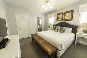 A bedroom with a bed, bench, two bedside tables, a TV, and a door.