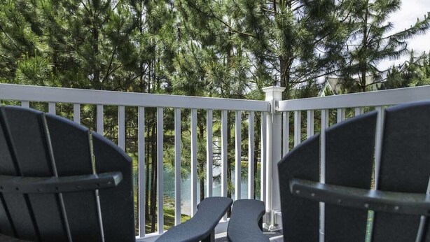 Una terraza con dos sillas Adirondack mirando un cuerpo de agua, rodeada de altos árboles de hoja perenne.