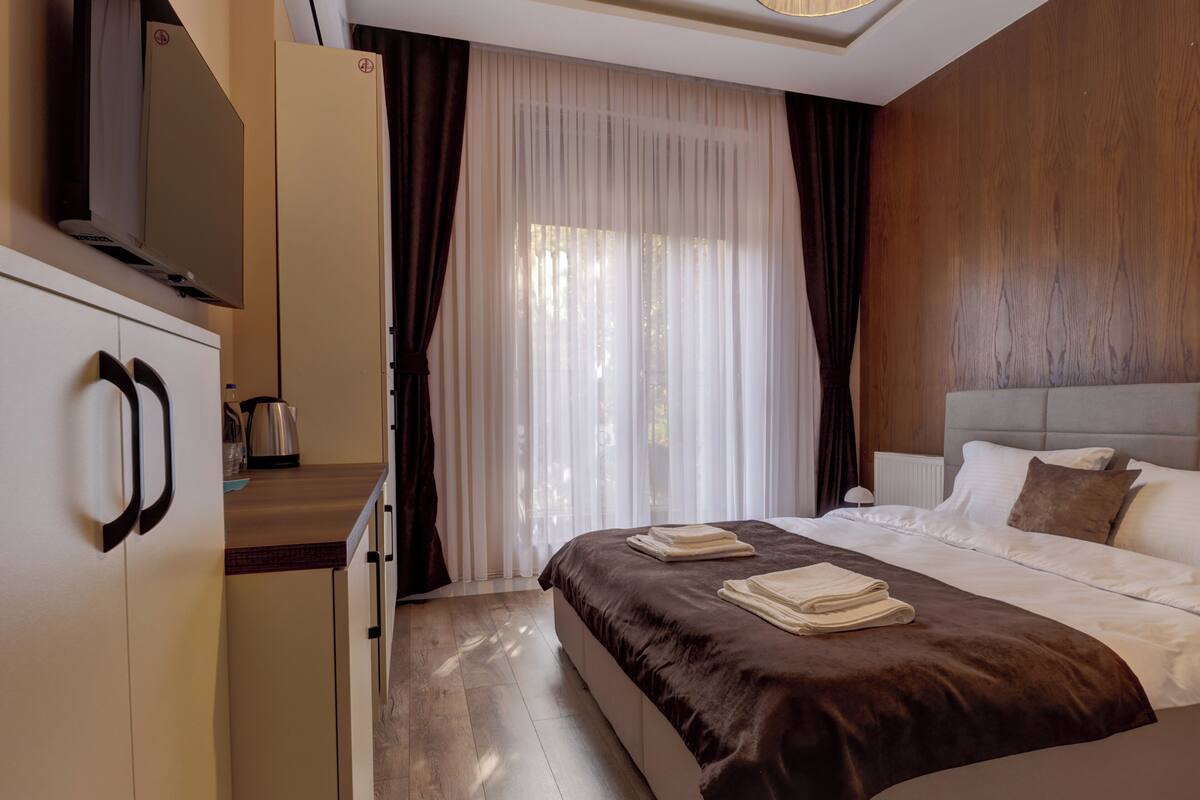 Een hotelkamer met een bed, een kledingkast, een televisie en een raam met gordijnen.