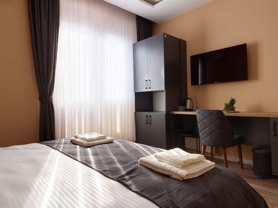 A hotel room with a bed, a desk, a chair, a TV, and a wardrobe.