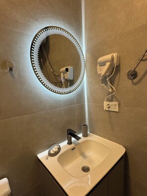 Een badkamer met een wastafel, een wasbak, een spiegel met LED-verlichting, een haardroger en een handdoekhouder.