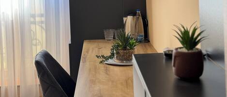 A modern room with a wooden table, a black TV mounted on the wall, a potted plant, and a window with sheer curtains.