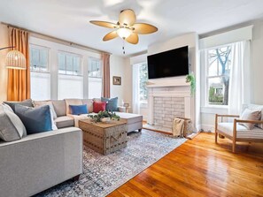 A living room with a sofa, a coffee table, a fireplace, and a TV mounted on the wall.