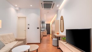 A modern living room with a sofa, a small table, a TV, and a kitchen area in the background. - Emma's Central Suite (Kos)