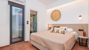 A bedroom with a large bed, a sliding glass door, a round wall decoration, and a small bedside table with a vase. - Emma's Central Suite (Kos)